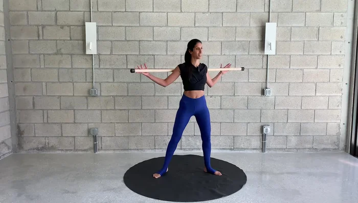 Feet wide apart. Hinge forward, holding the stick in front of your chest. Rotate your spine side to side, pivoting on your back leg and allowing your heel to lift.
