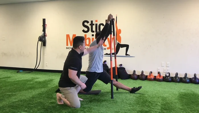Hold resistance sticks at the 11:01 hand rope top position. Add about 30% tension by pushing the sticks down into the floor, activating the lats.