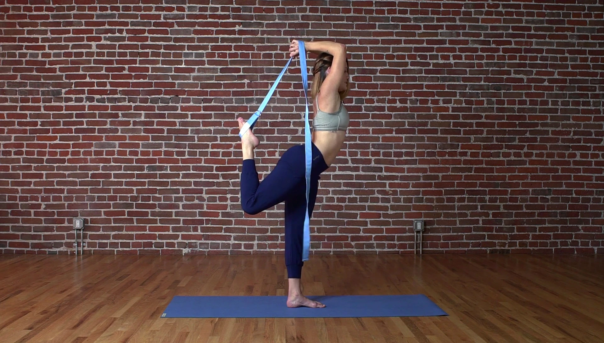 Woman performing Natarajasana with the yoga strap.
