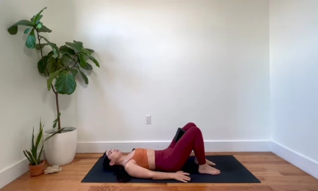 Woman performing a glute bridge, squeezing the yoga block between her thighs.