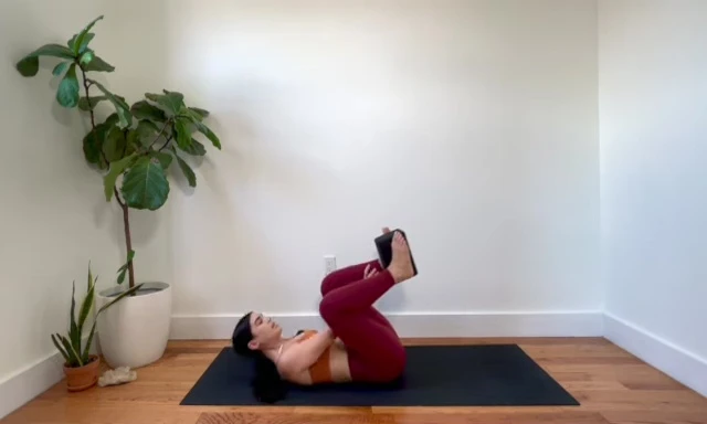 Woman in tabletop position with a yoga block between her ankles, preparing for leg extensions.