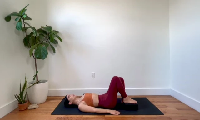 Woman performing bridge movement with yoga block under one foot.