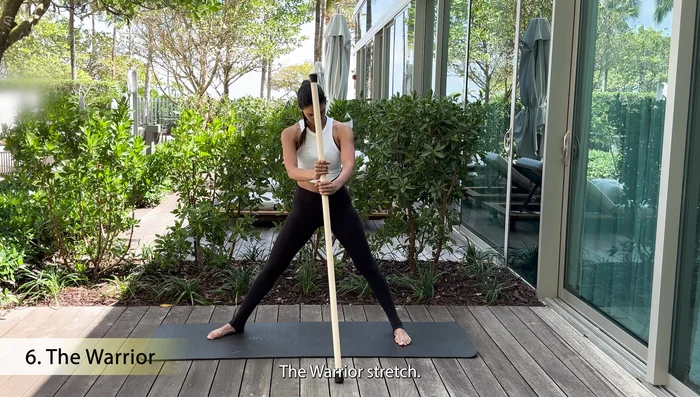 Place the stick behind your lower back, turn out one foot, and bend the knee.